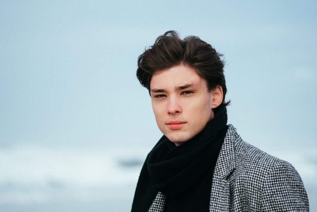 Young man in winter fashion standing at the beach with a calm expression.
